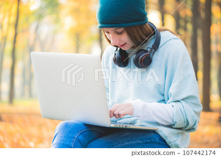 Smiling teenage girl sitting on bench with laptop 107442174