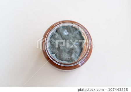 Open jar with sweet jam and mold on a white background. Mold in a jar of raspberry jam. Hazardous to health. Open jar with sweet jam and mold on a white background. Mold in a jar of raspberry jam. Hazardous to health. 107443228