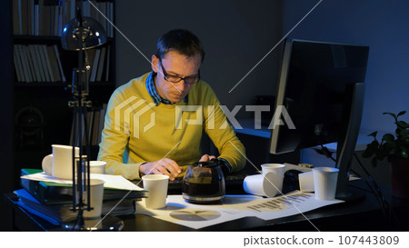 Young busy man typing on computer keyboard while working overtime in night office 107443809