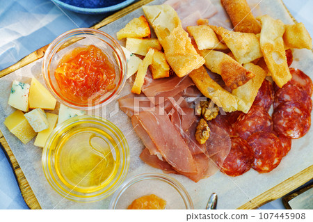 A wooden tray with chips, honey, sauce, cheese and meat appetizers A wooden tray with chips, honey, sauce, cheese and meat appetizers 107445908