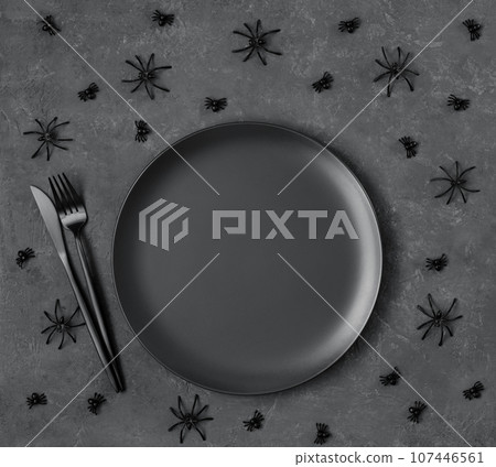 Halloween black table setting with spiders. Empty black plate, cutlery. spiders on dark gray background. Halloween festive serving. Copy space, top view, flat lay. Halloween black table setting with spiders. Empty black plate, cutlery. spiders on dark gray background. Halloween festive serving. Copy space, top view, flat lay. 107446561