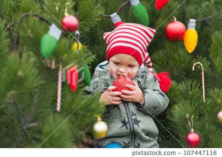 Cute toddler holding christmas ball in decorated backyard close-up and copy space. Happy celebration 107447116