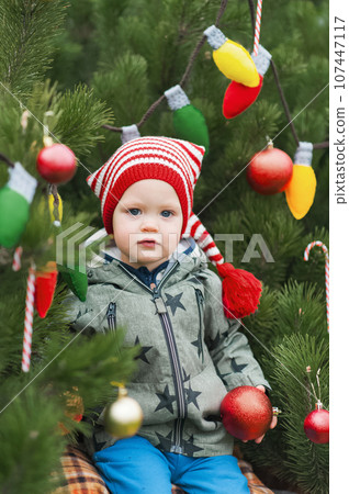 Cute toddler holding christmas ball in decorated backyard close-up and copy space. Happy celebration 107447117