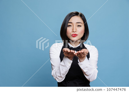 Smiling attractive asian waitress wearing uniform sending air kiss and looking at camera. Beautiful young woman receptionist expressing love and affection portrait in studio Smiling attractive asian waitress wearing uniform sending air kiss and looking at camera. Beautiful young woman receptionist expressing love and affection portrait in studio 107447476