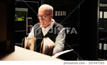 Private inspector review case files, reading confidential reports to evaluate evidence authenticity in police agency archive. Detective conducting investigation, inspecting documents for discovery. 107447563