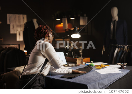 Professional couturier manufacturing business suit bespoken piece, looking online for inspiration. Experienced suitmaker working in exquisite atelier shop, creating premium quality custom made garment 107447602