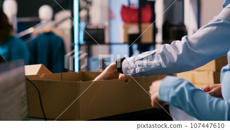 Diverse employees working at customers orders, putting fashionable clothes in carton boxes in clothing store. Boutique workers preparing packages for delivery in shopping mall. Fashion concept 107447610