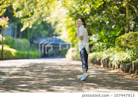 Smiling young woman in sportswear walking through greenery Smiling young woman in sportswear walking through greenery 107447913