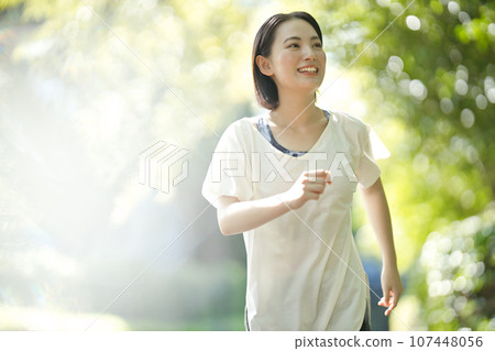 Smiling young woman in sportswear walking through greenery 107448056