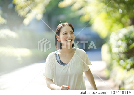 Smiling young woman in sportswear walking through greenery Smiling young woman in sportswear walking through greenery 107448119