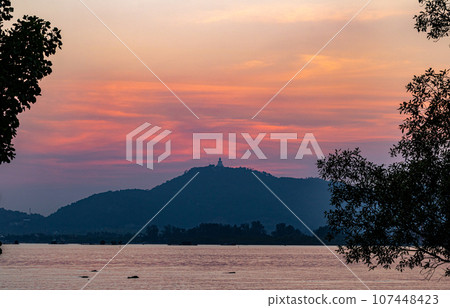 scenery yellow sky glare of sun above Phuket big Buddha.Phuket Big Buddha is one of the island most important and revered landmarks on the island..image for travel and culture concept. scenery yellow sky glare of sun above Phuket big Buddha.Phuket Big Buddha is one of the island most important and revered landmarks on the island..image for travel and culture concept. 107448423