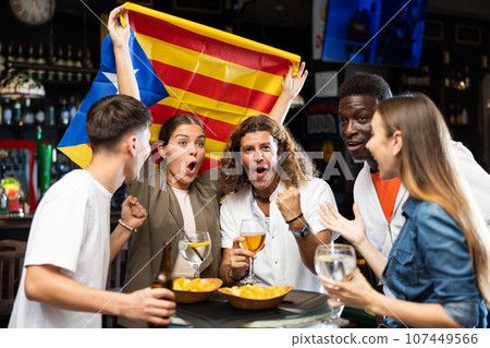 Happy international sport supporters holding up the flag of Estelada with beer and chips in the pub Happy international sport supporters holding up the flag of Estelada with beer and chips in the pub 107449566