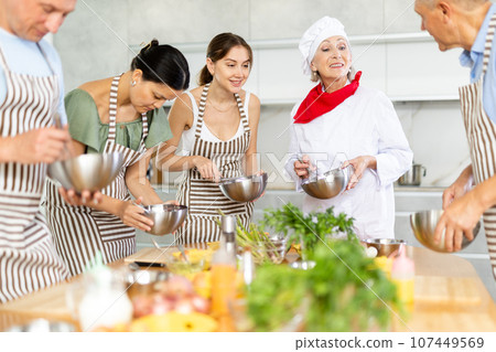 Elderly woman professional chef conducting group culinary courses Elderly woman professional chef conducting group culinary courses 107449569