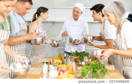 Smiling old man chef of cooking course teaching attendees how to mix sauce 107449649