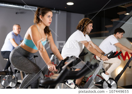 Man and woman taking indoor cycling class at fitness center, doing cardio riding bike 107449655