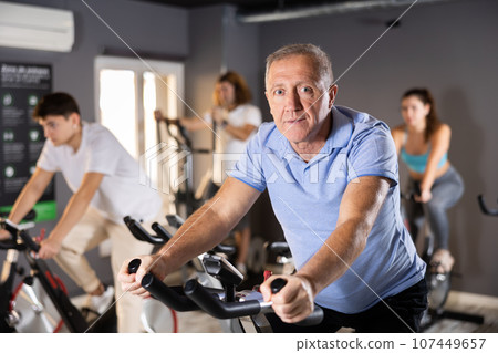 Aged man doing cardio workout on exercise bike in gym 107449657