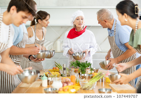 Smiling old woman chef of cooking course teaching attendees how to mix sauce 107449707