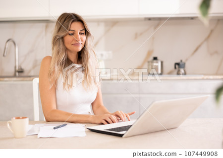 Woman chatting on internet using a laptop in kitchen 107449908