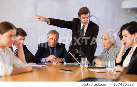 Portrait of angry male boss in business suit pointing to the door to his subordinate during meeting forcing him 107450158