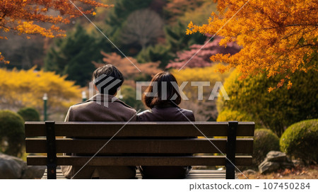 Rear view of a couple sitting on a bench in an autumn park 107450284