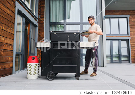 A man cooks on a grill on the veranda. A man cooks on a grill on the veranda. 107450616