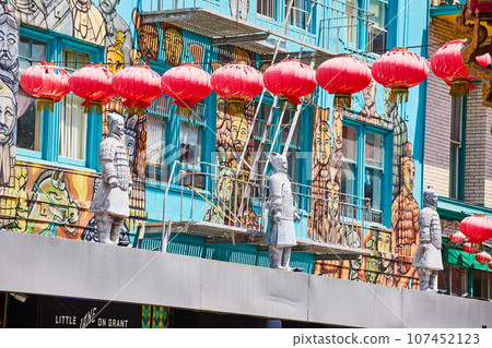 Red paper lanterns hanging in front of Chinese wall mural with soldier statues 107452123
