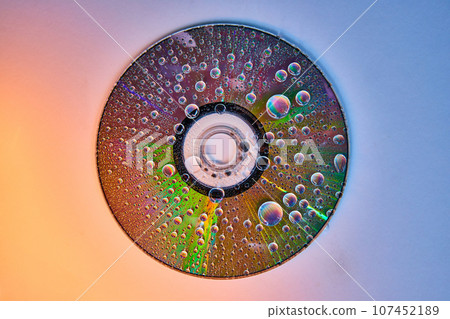 CD on gradient shift background with rainbow water drops on reflective metal surface 107452189
