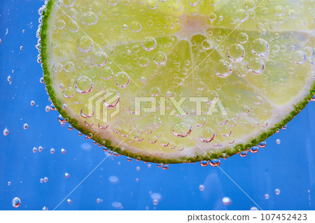 Macro shot of green lime slice on blue background with fizzy bubbles 107452423