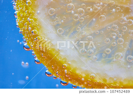 Macro of fizzy bubbles on lemon slice against blue background Macro of fizzy bubbles on lemon slice against blue background 107452489