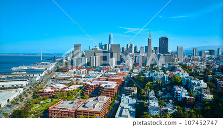 Aerial apartment buildings leading to heart of downtown skyscrapers with view of Oakland Bay Bridge Aerial apartment buildings leading to heart of downtown skyscrapers with view of Oakland Bay Bridge 107452747