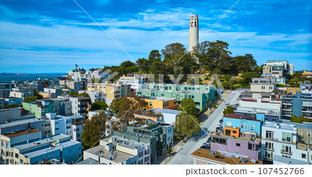 Coit Tower atop Telegraph Hill overlooking houses and apartments on hill with blue sky aerial Coit Tower atop Telegraph Hill overlooking houses and apartments on hill with blue sky aerial 107452766