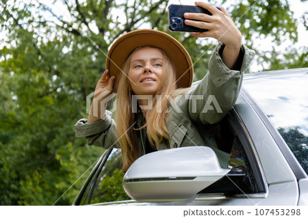 Blonde woman stoped car on road to take a selfie photo. Young tourist explore local travel making candid real moments. True emotions expressions of getting away and refresh on open air Blonde woman stoped car on road to take a selfie photo. Young tourist explore local travel making candid real moments. True emotions expressions of getting away and refresh on open air 107453298