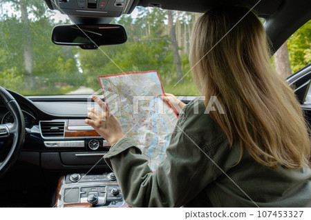 Smiling young woman sitting in car on road check the route on travel map. Local solo travel on weekends concept. Exited woman explore freedom outdoors in forest. Unity with nature lifestyle, rest 107453327