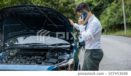 Middle-aged businessman calling roadside assistance for car breakdown. Horizontal photo of elegant man in suit standing on highway, looking worried and frustrated. Concept for transportation problems. 107453696