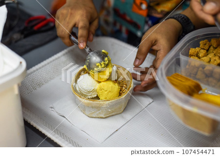 Hand holding coconut and mango ice cream in coconut shell in Jalan Alor street food market in Kuala Lumpur Hand holding coconut and mango ice cream in coconut shell in Jalan Alor street food market in Kuala Lumpur 107454471