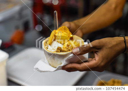 Hand holding coconut and mango ice cream in coconut shell in Jalan Alor street food market in Kuala Lumpur Hand holding coconut and mango ice cream in coconut shell in Jalan Alor street food market in Kuala Lumpur 107454474