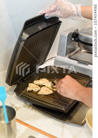 Chef frying chicken meat in butter in electric griller Chef frying chicken meat in butter in electric griller 107454498