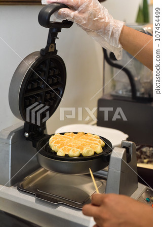 the cook check the dough for sweet waffles into the waffle iron with a wooden stick the cook check the dough for sweet waffles into the waffle iron with a wooden stick 107454499