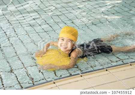 A girl swimming with a beat board in the pool A girl swimming with a beat board in the pool 107455912