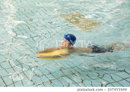 一個男孩在泳池裡拿著拍板游泳 107455949