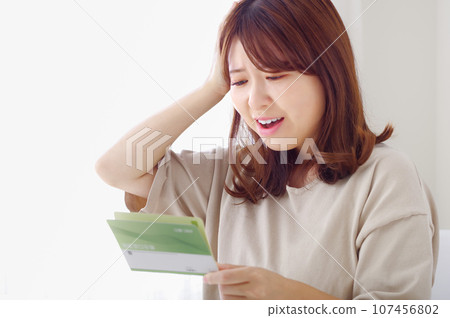 A woman makes a sad expression while looking at her savings passbook A woman makes a sad expression while looking at her savings passbook 107456802