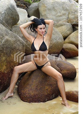 Slender sexy ukrainian 37 years old woman in black bikini sitting on the stones and holding her hair 107457309