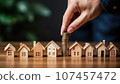 Businessman putting coin to stack of coins with wooden house model on wooden table, Saving money for buy house concept. 107457472