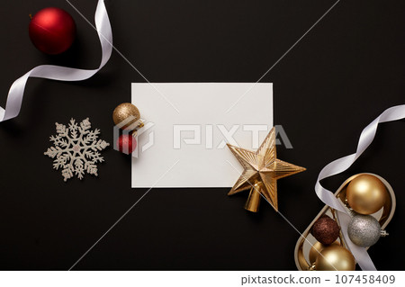 Blank paper decorated with colorful baubles, a star, snowflakes and white ribbons. Empty space on the paper for text adding. Holiday illumination and decoration concept 107458409