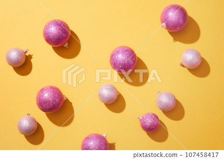 A lot of blinking baubles in pink color are arranged over the yellow background. Christmas is often seen as a magical time that associated with a sense of hope 107458417