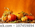 Colorful display of pumpkins, autumn leaves sitting in a row on woodentable, orange background 107459894