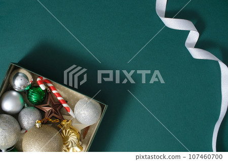 Christmas decoration composition on dark green background with a small gift box filled with beautiful baubles and silver ribbon. Creative background for advertising and space for design Christmas decoration composition on dark green background with a small gift box filled with beautiful baubles and silver ribbon. Creative background for advertising and space for design 107460700