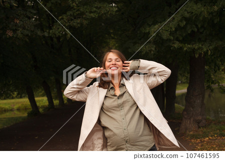 Cheerful young pregnant woman smiling and walking in park, portrait Cheerful young pregnant woman smiling and walking in park, portrait 107461595