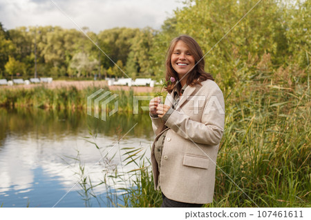 Happy pregnant woman with wild flower, outdoor portrait 107461611
