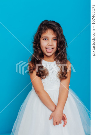 a little girl in a white dress shows her tongue on a blue background a little girl in a white dress shows her tongue on a blue background 107463172